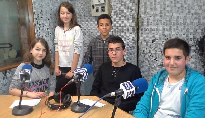 foto de un estudio de radio en el que hay 5 niños y niñas frente a los micrófonos