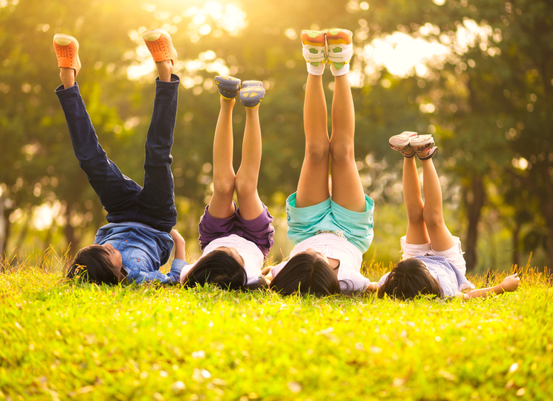 Grupo de 4 niños felices tendidos sobre césped verde al aire libre en el parque