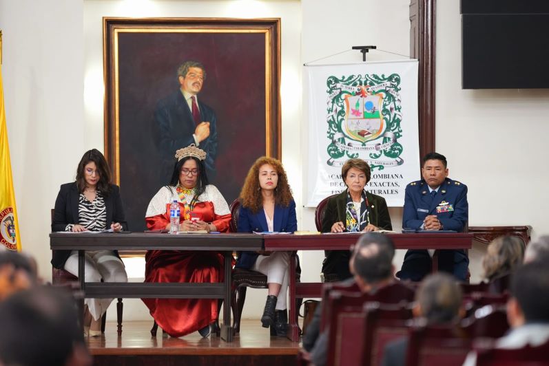 Foto de 4 mujeres y un hombre sentados en una mesa mirando al publico que los escucha.Fondo cuadro de Luis Carlos Galán