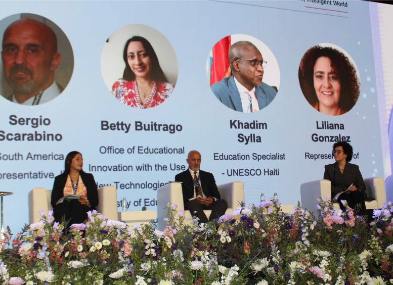 Betty Buitrago y dos personas más en el panel, en un auditorio con fondo que muestra las fotos de los participantes