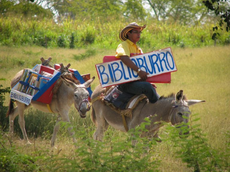Foto de Luis Soriano sobre un burro con el letrero Biblioburro y detrás otro burro cargado de libros