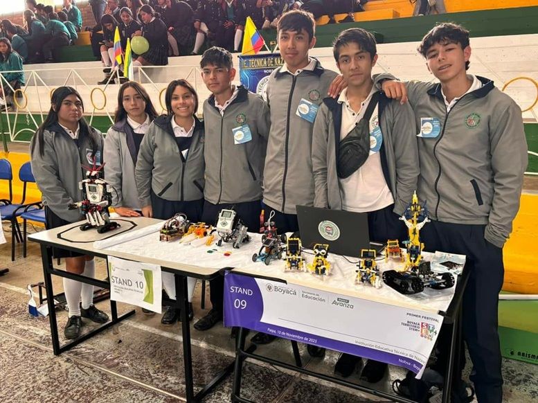 siete jovenes estudiantes de colegio uniformados, posan detrás de la mesa con las muestras de su trabajo 