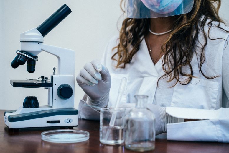 Foto de un microscopio, tubo de ensayo y otros elementos de laboratorio, y una mujer de pelo largo y bata blanca