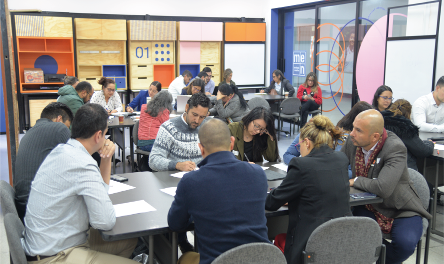 Foto de varios hombres y mujeres sentados en mesas de trabajo en un salón