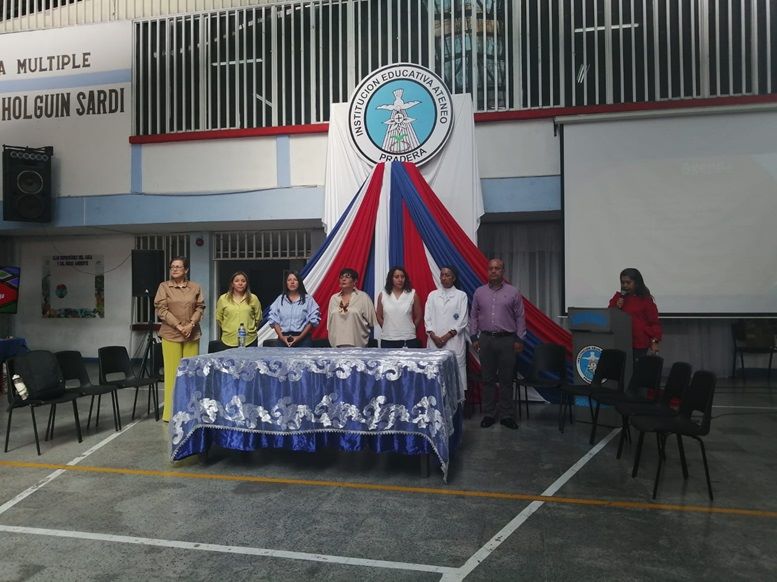 Foto de varios adultos en una ceremonia, con letrero detrás que dice Institución Educativa Ateneo Pradera