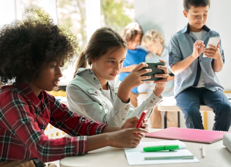 Tres adolescentes en aula de clases mirando sus teléfonos celulares