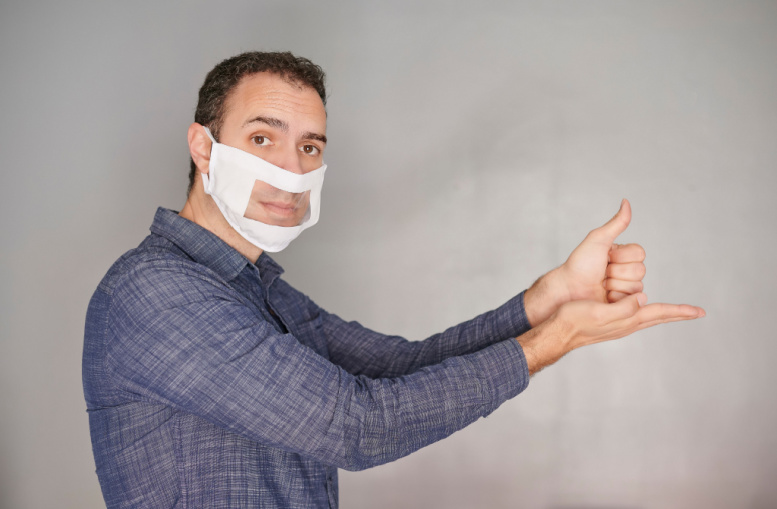 Foto de hombre con una mascarilla de sordomudo, mostrando el gesto de ayuda en lengua de señas