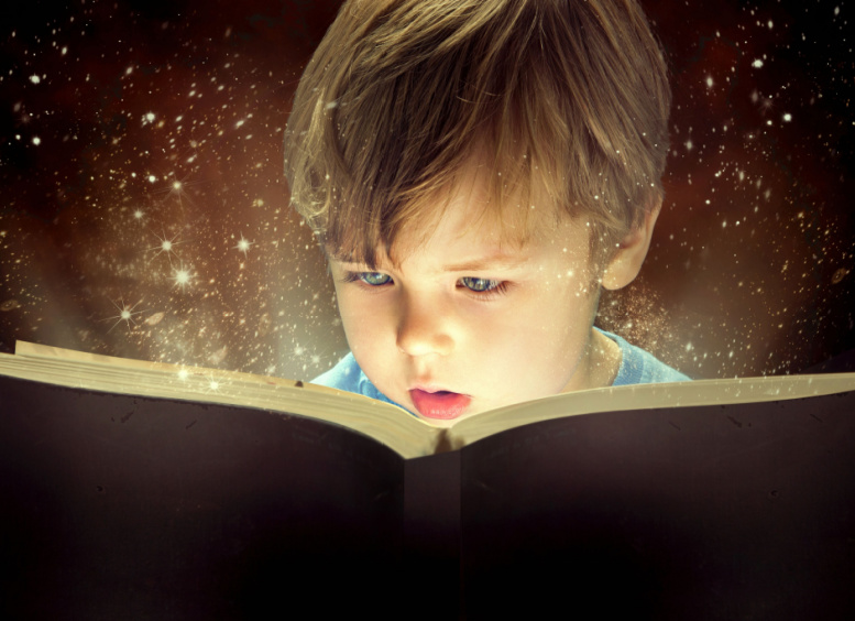 Niño de seis años, con la boca abierta absorto leyendo libro del que salen destellos que le ilumina el rostro