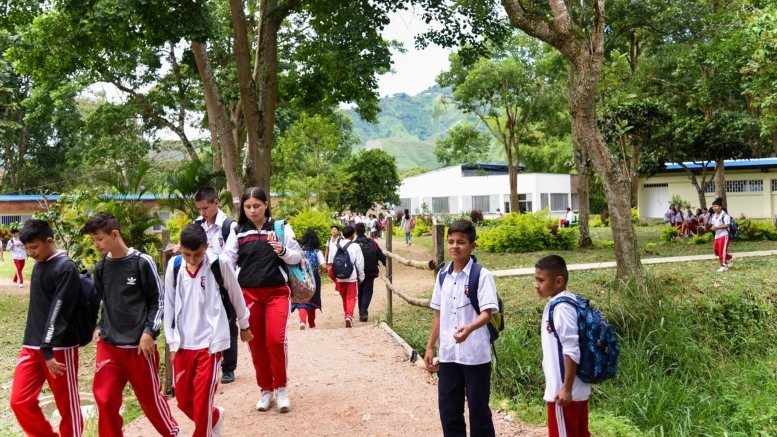 Foto de varios niños y niñas con unifome en el exterior de escuela rural, con árboles y montañas