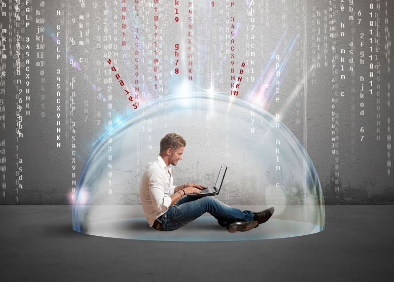 Hombre sentado en el piso con un computador, cubierto por un domo transparente que lo protege de ataques cibernéticos
