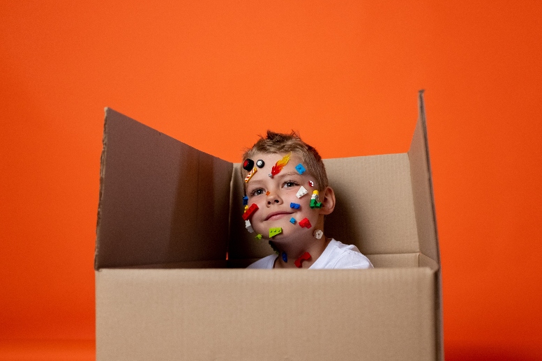 Niño escondido entre una caja de cartón, sonriente, con varias pegatinas en la cara