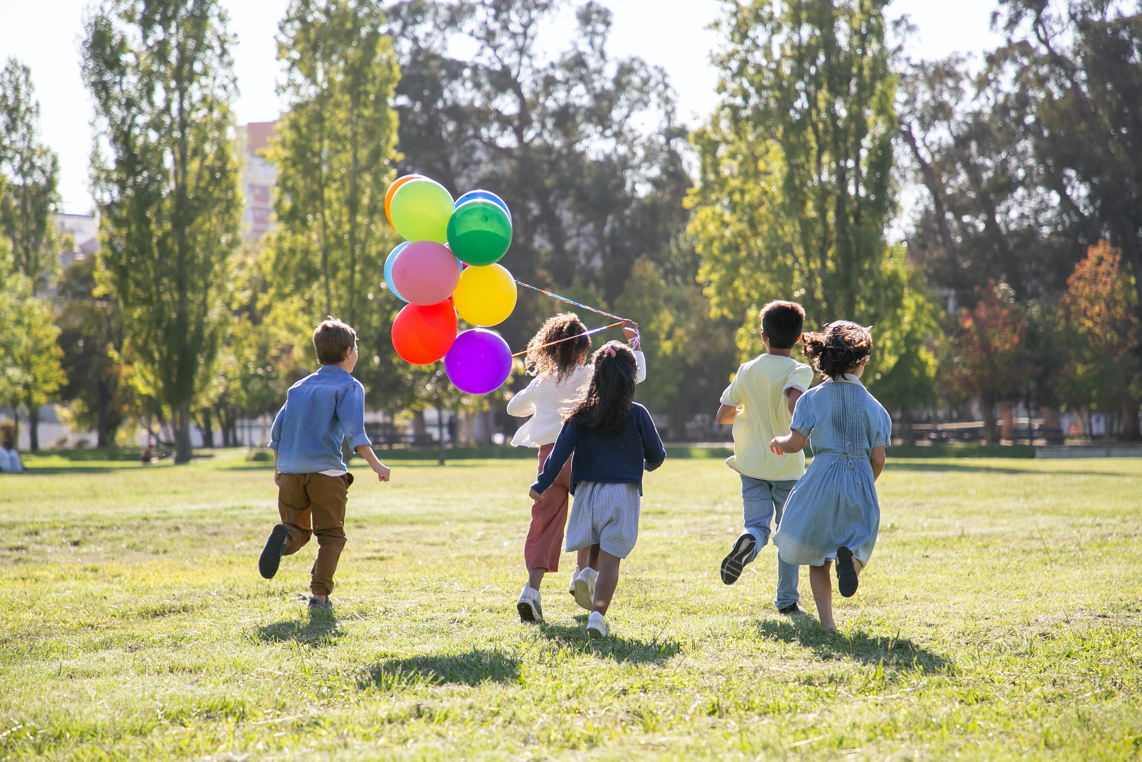 tres niñas y dos niños corren por el campo con globos, dando la espalda a la cámara