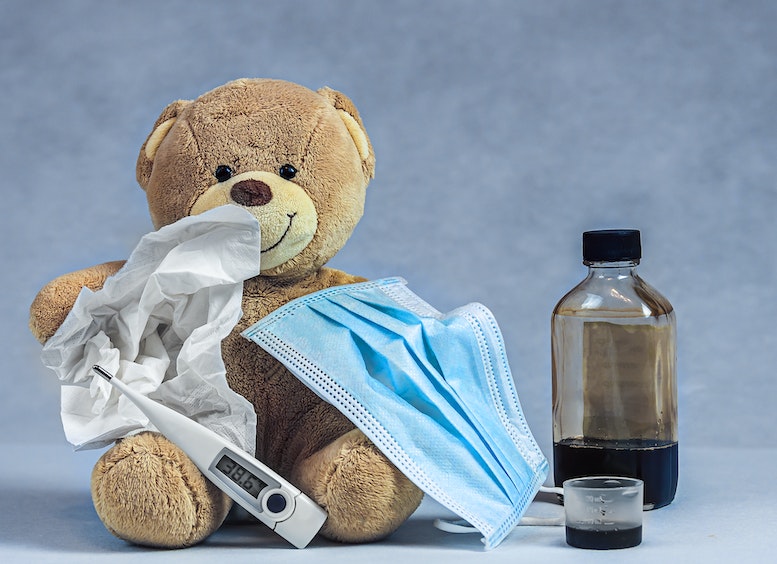Oso de peluche rodeado de tapabocas, termómetro, kleenex, jarabe
