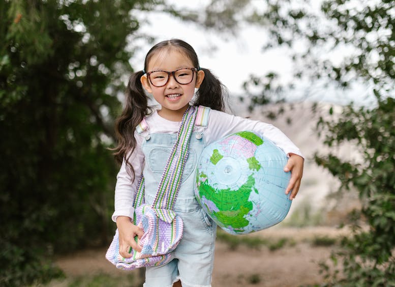 Foto de niña de seis años, con gafas que sonríe y sostiene un globo terráqueo en su brazo
