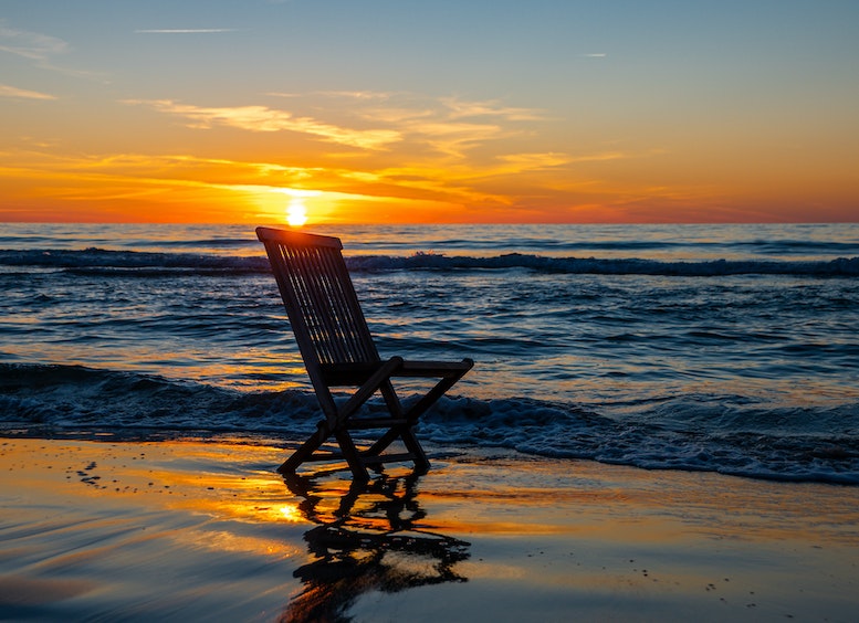 Foto de un atardecer con el océano y una silla desocupada mirando al mar