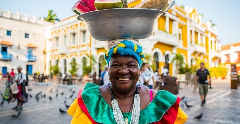 foto de una mujer palenquera y de fondo está el carnaval de Barranquilla