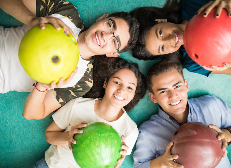 Foto de adolescentes multiétnicos mostrando bolas de colores, acostados en el piso y sonriendo