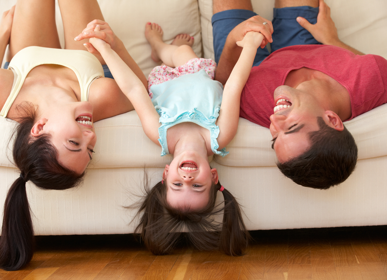 padre, madre e hija, acostados sobre un sofá con la cabeza hacia el piso y los pies arriba, riendo