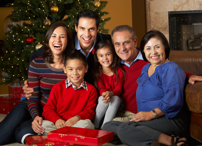 Familia de varias generaciones riendo sentadas frente al Árbol De Navidad