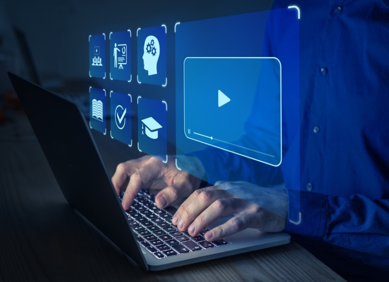 manos de hombre tecleando un computador portátil. De este salen diversas pantallas que se proyectan sobre la camisa del hombre, y que muestran diversos símbolos alusivos a video, educación, libros, docentes, entre otros