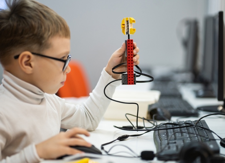 Niño pequeño con gafas, enfrente de computador construye y programa Lego Robot WeDo