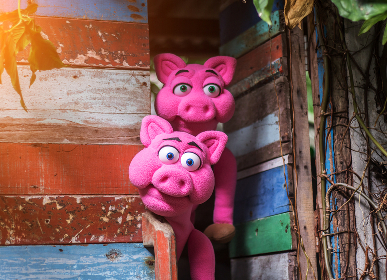 Dos títeres, cerdos rosados, asomando por puerta de madera de colores