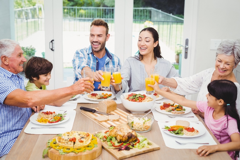 abuelos, padres y nietos brindando con jugo de naranja, sentados alrededor de la mesa para almorzar