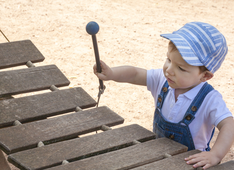 Foto de niño de tres años vestido de azul, que eleva la mano para tocar una marimba