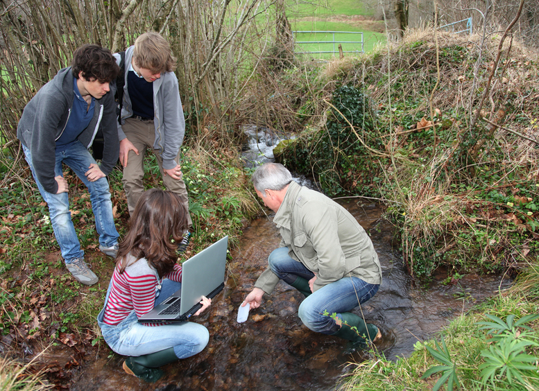 Tres jóvenes con un maestro en temas de educación ambiental en un campo