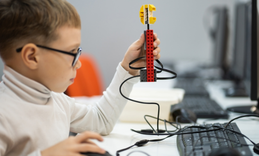 Niño pequeño con gafas, enfrente de computador construye y programa Lego Robot WeDo