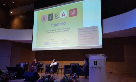 Foto del auditorio con los panelistas y una pantalla en el fondo con el título STEAM más género