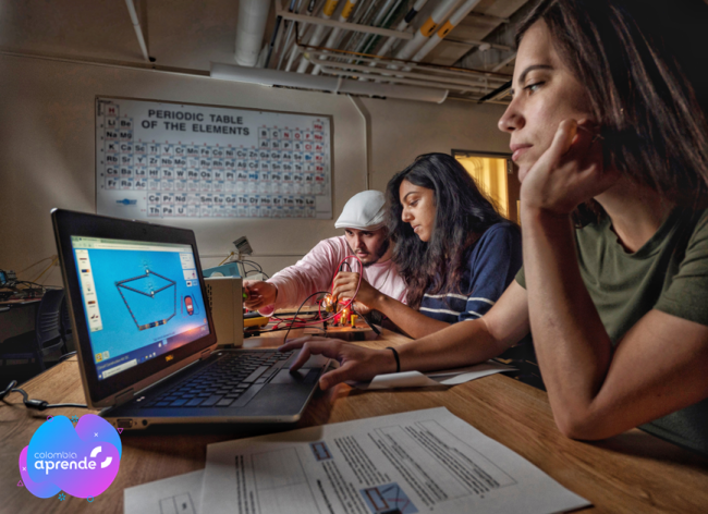 Foto de dos estudiantes mujeres y un estudiante hombre trabajando en mesa frente a computador con simulaciones