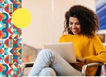 Foto de una mujer sentada trabajando con un portátil y sonriendo