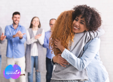 Foto de dos mujeres abrazadas. Tres personas aplauden atrás y sonríen